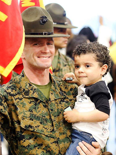 A uniformed Marine holds a young boy