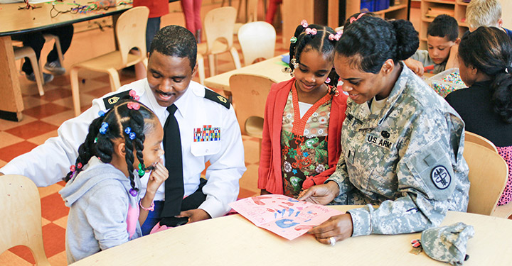 A uniformed service couple sit with their children in a child care center
