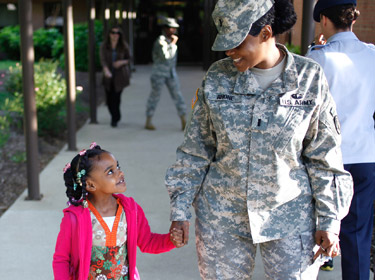 Female serviceperson holds a young girl's hand as they walk