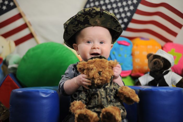 Baby holding a teddy bear wearing a uniform