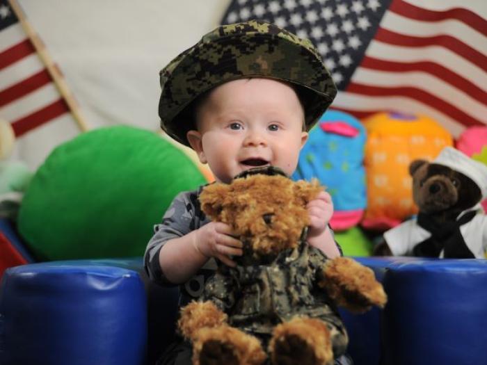 Baby holding a teddy bear wearing a uniform